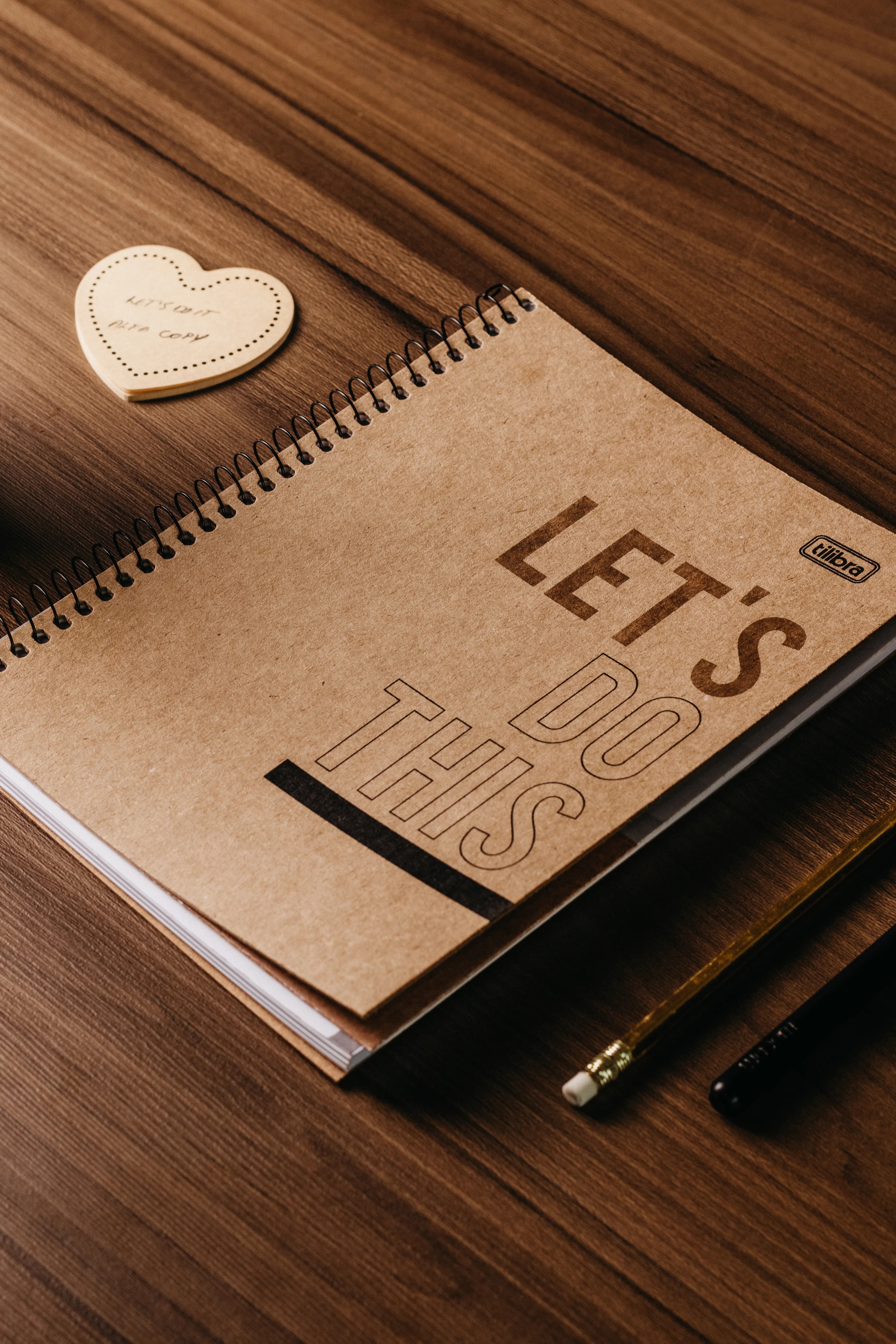 A kraft spiral notebook and pencils on a wooden desk